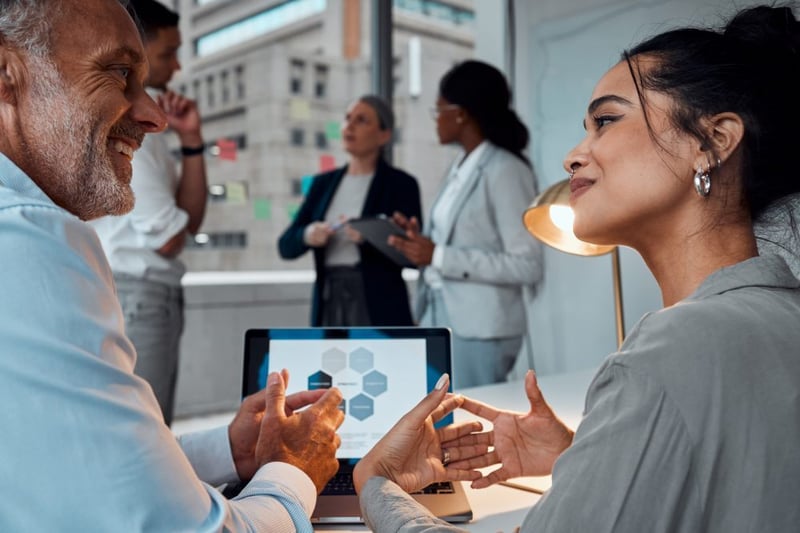 Dos profesionales en una oficina moderna analizando datos en un portátil para mejorar las prácticas de convertir clientes usando agencias HubSpot.