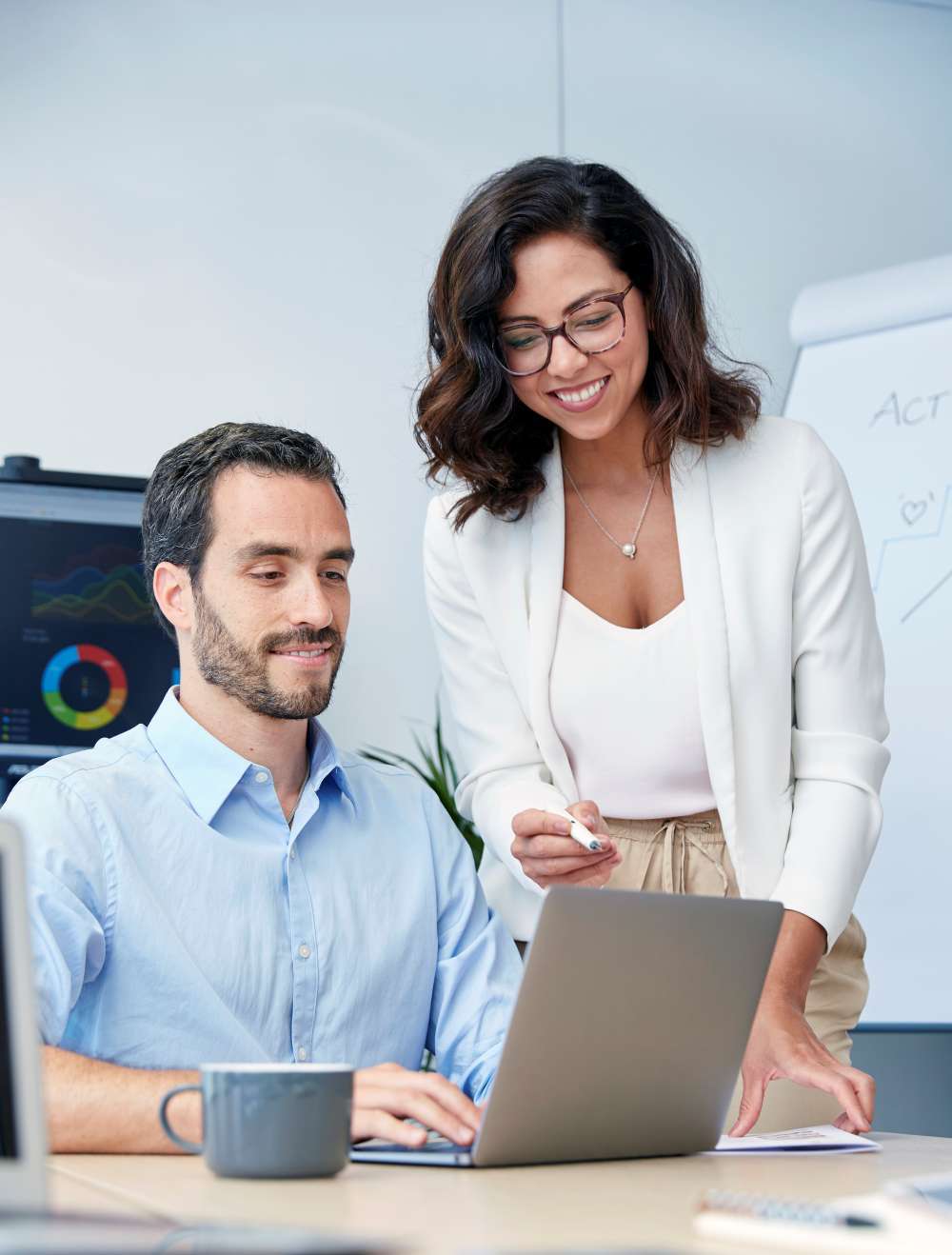Dos profesionales en una oficina revisando datos de marketing en un monitor.