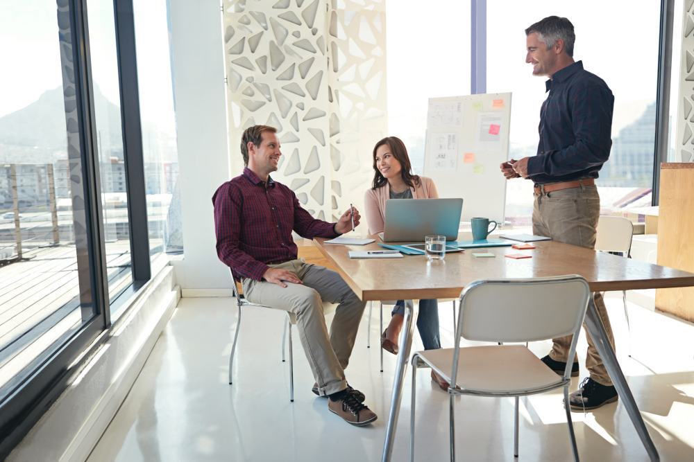 Tres profesionales en una oficina corporativa de Madrid sonriendo y celebrando frente a un monitor de laptop, mostrando colaboración en crecimiento B2B.