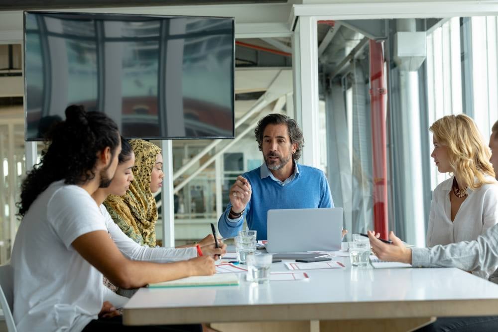 Un hombre sentado a una mesa de oficina discutiendo con varias personas sobre cómo alinear ventas y marketing con HubSpot