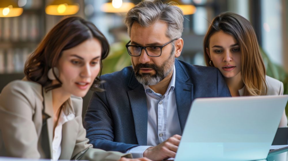 Un hombre y dos mujeres en una oficina analizando datos en un monitor sobre procesos de seguros.