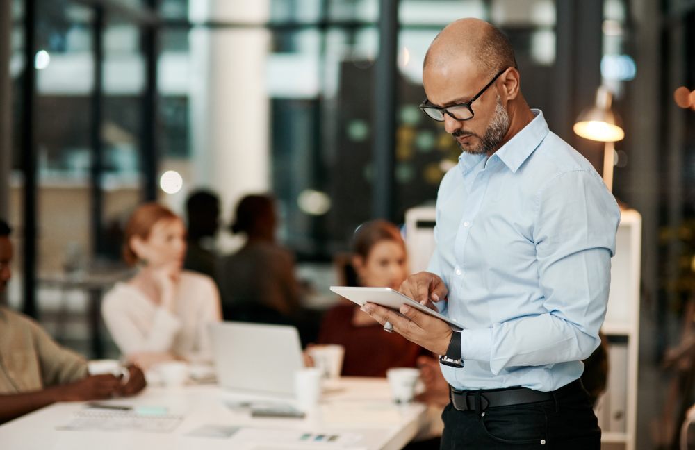 Un consultor senior con gafas y camisa azul está de pie analizando datos en su tableta para elegir una agencia HubSpot certificada 
